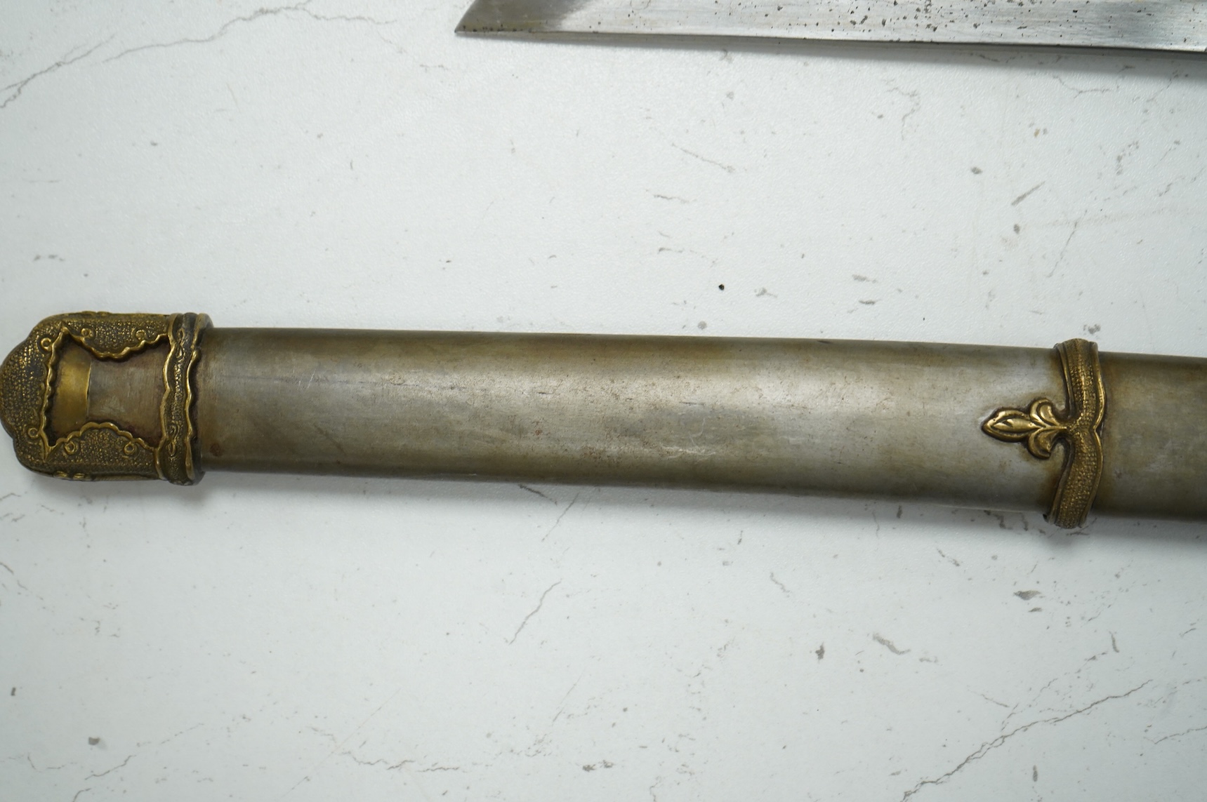 A Japanese World War II NCO’s sword katana with regulation blade and hilt with tape bound fish skin covered grip, and brass mounts, in its steel scabbard